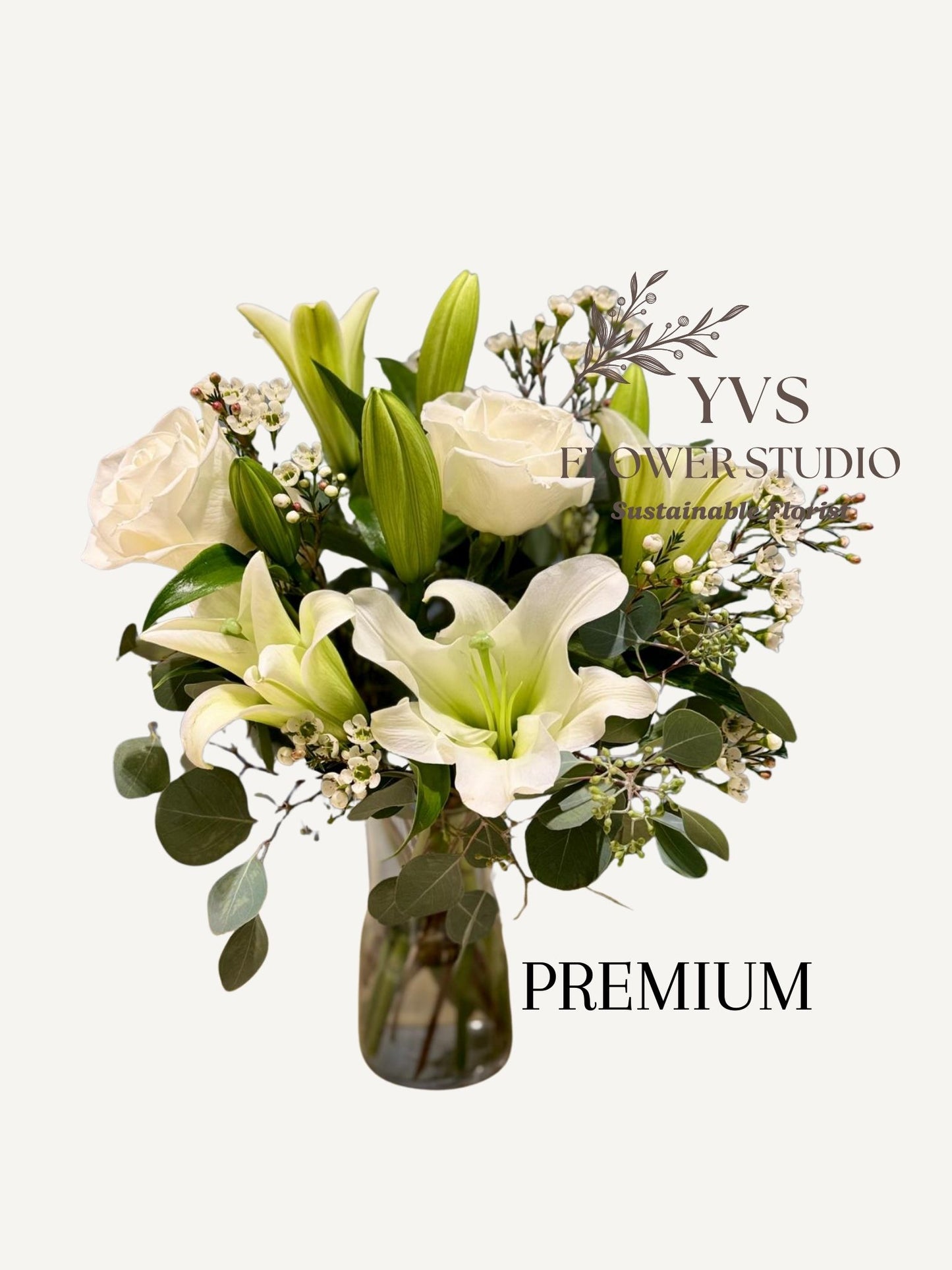Bouquet of white lilies and roses with greenery in a clear vase, branded 'YVS Flower Studio'.