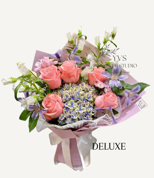 Bouquet of blue two tone hydrangea and other flowers wrapped in lilac paper with 'VS Florist Studio' branding.