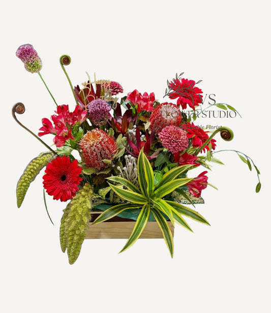 A table top arrangement consisting of a vibrant mix of red and green flowers and foliage